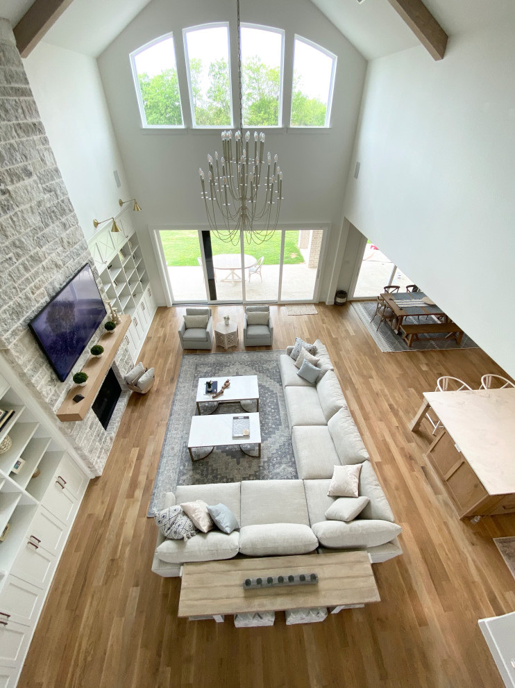 Immagine di un ampio soggiorno nordico aperto con pareti bianche, parquet chiaro, cornice del camino in pietra, TV a parete, pavimento beige e travi a vista
