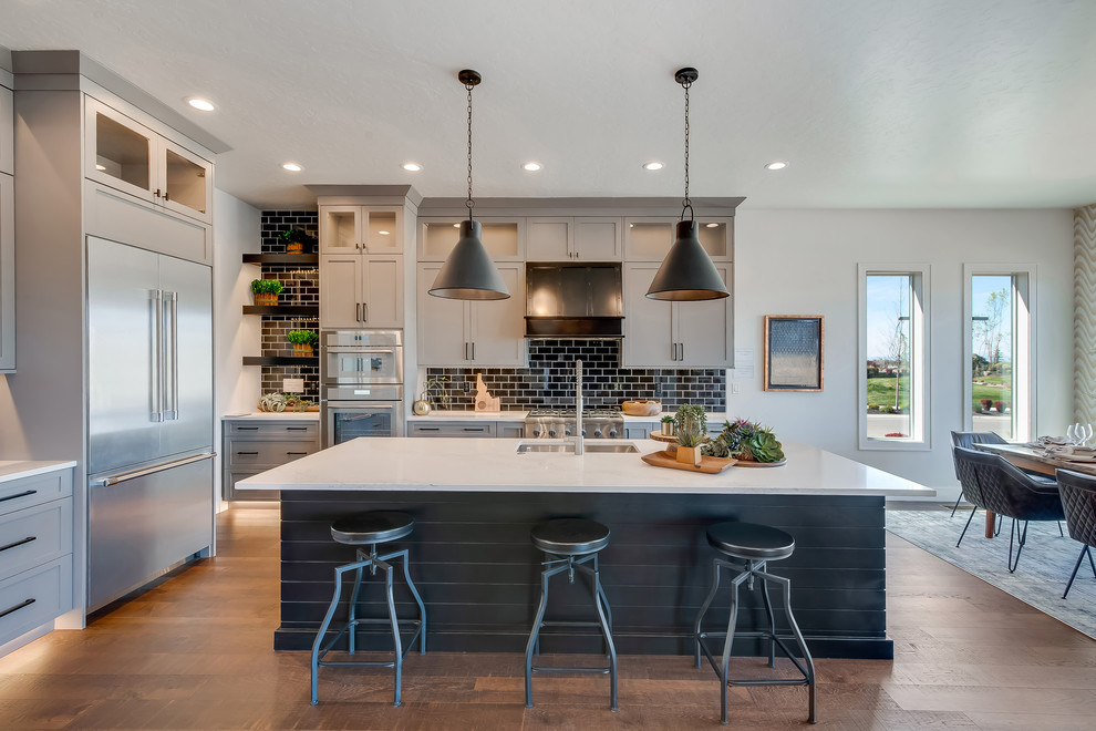 Inspiration for a large transitional u-shaped eat-in kitchen in Boise with an undermount sink, shaker cabinets, grey cabinets, black splashback, subway tile splashback, stainless steel appliances, medium hardwood floors, with island, brown floor, white benchtop and quartz benchtops.