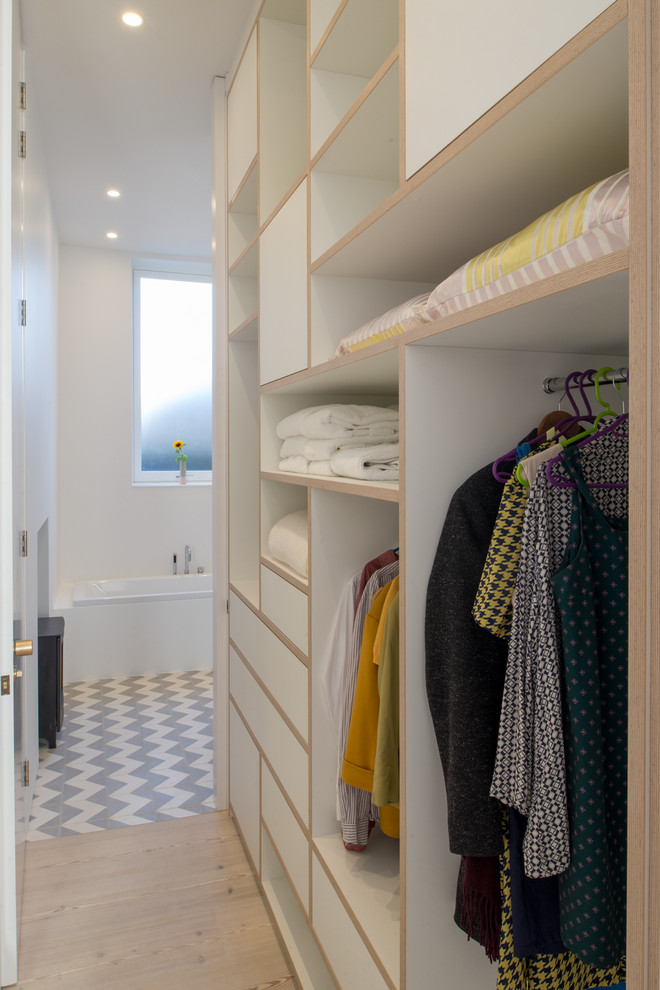 Photo of a mid-sized scandinavian gender-neutral storage and wardrobe in London with open cabinets, white cabinets, light hardwood floors and beige floor.