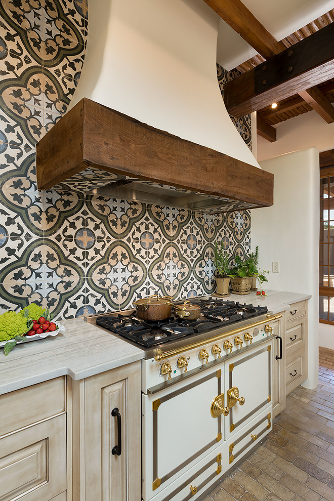 Inspiration for a mid-sized mediterranean u-shaped eat-in kitchen in Other with a farmhouse sink, raised-panel cabinets, quartzite benchtops, panelled appliances, brick floors, with island and beige floor.