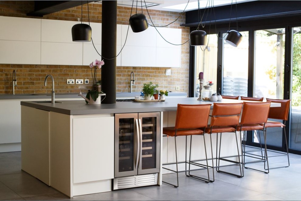 Inspiration for a mid-sized industrial single-wall kitchen in London with a drop-in sink, flat-panel cabinets, white cabinets, concrete benchtops, brick splashback, porcelain floors, with island, grey floor, grey benchtop, beige splashback and stainless steel appliances.