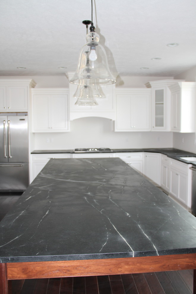 Example of a large mountain style galley dark wood floor eat-in kitchen design with a drop-in sink, beaded inset cabinets, white cabinets, soapstone countertops, white backsplash, stainless steel appliances and an island