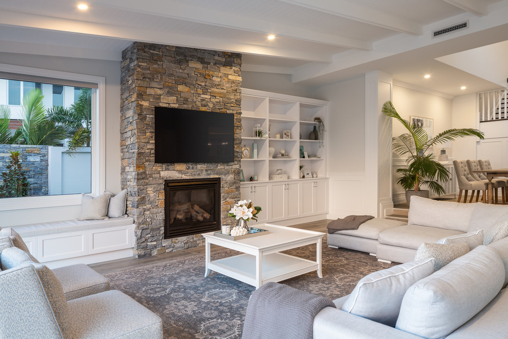Photo of a large beach style open concept living room in Gold Coast - Tweed with grey walls, medium hardwood floors, a standard fireplace, a stone fireplace surround, a wall-mounted tv and brown floor.