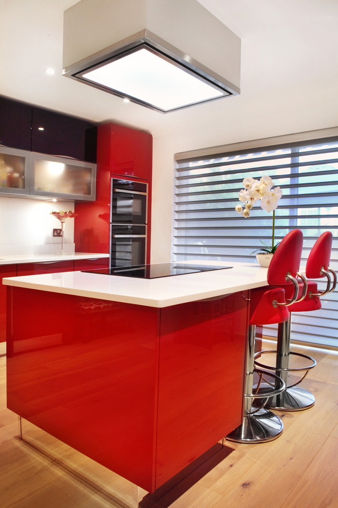 Inspiration for a mid-sized contemporary single-wall eat-in kitchen in Buckinghamshire with red cabinets, quartzite benchtops, stainless steel appliances, light hardwood floors, with island, an integrated sink and flat-panel cabinets.