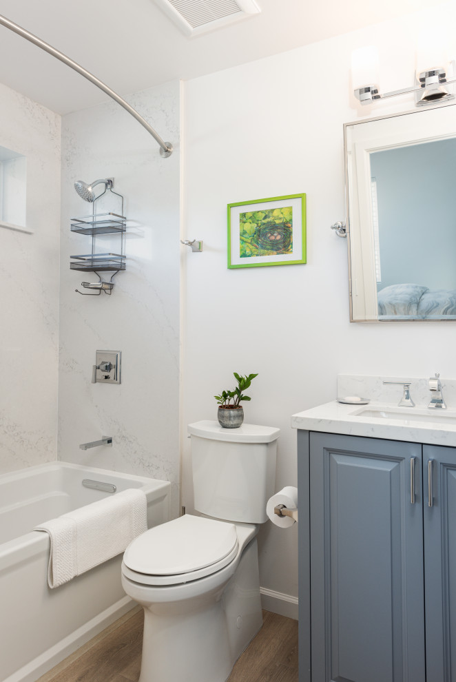 Пример оригинального дизайна: маленькая ванная комната в стиле неоклассика (современная классика) с фасадами с выступающей филенкой, синими фасадами, ванной в нише, душем над ванной, раздельным унитазом, белой плиткой, белыми стенами, полом из ламината, врезной раковиной, столешницей из искусственного кварца, бежевым полом, шторкой для ванной, белой столешницей, тумбой под одну раковину и встроенной тумбой для на участке и в саду