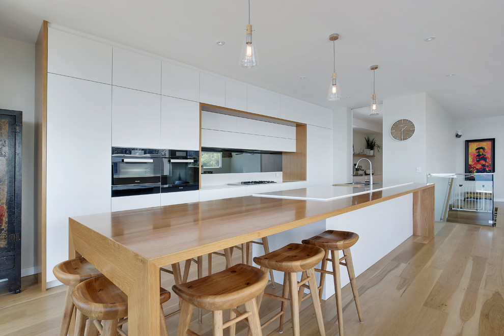 Design ideas for a large scandinavian kitchen in Sydney with a double-bowl sink, quartz benchtops, mirror splashback, black appliances and light hardwood floors.