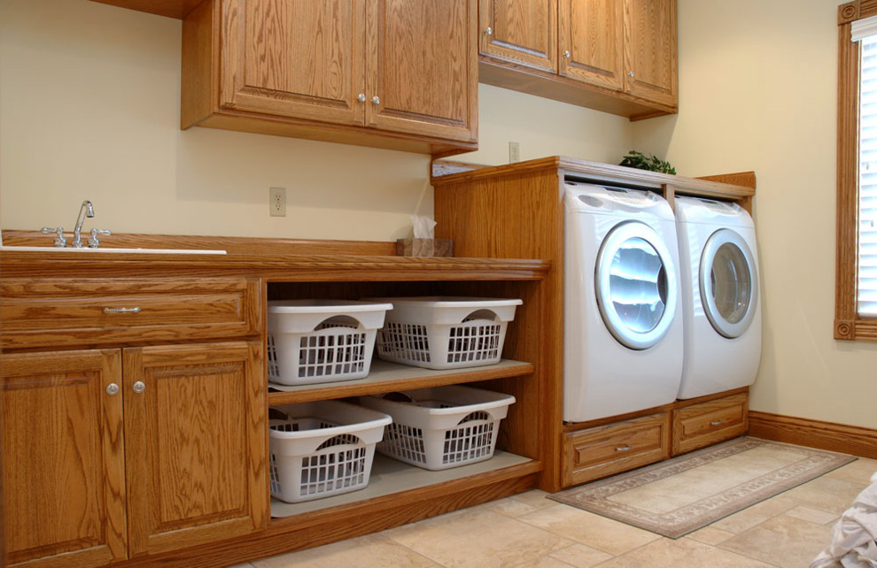 Mid-sized traditional single-wall laundry room in Cleveland with a drop-in sink, raised-panel cabinets, wood benchtops, beige walls, travertine floors, a side-by-side washer and dryer, beige floor and medium wood cabinets.