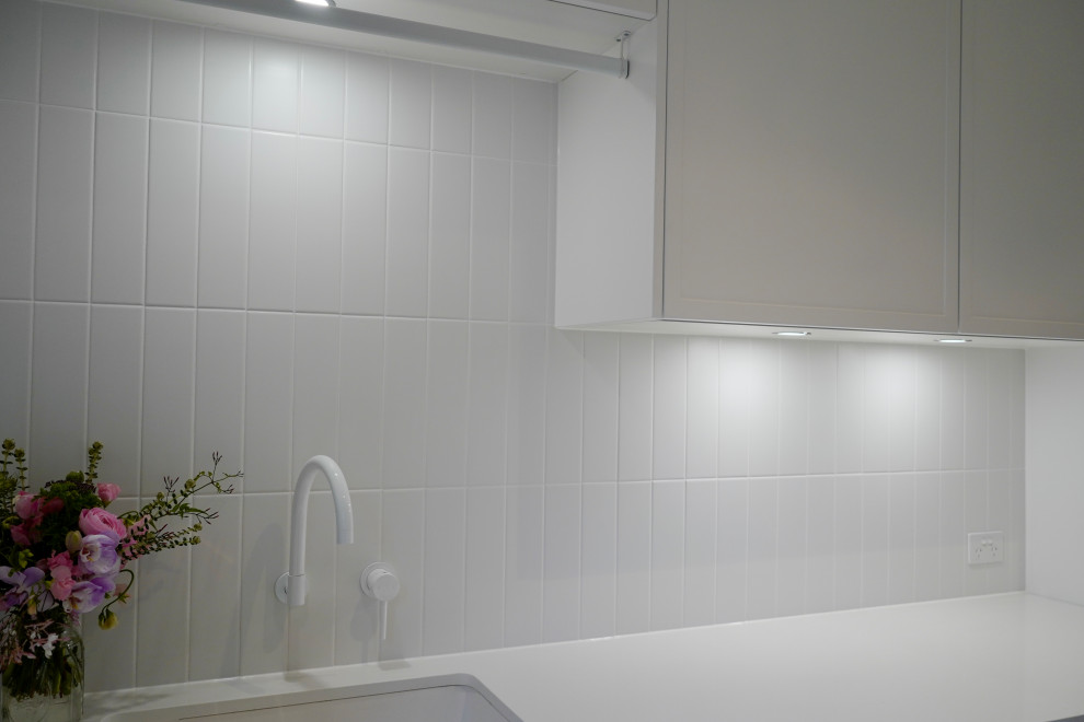 This is an example of a mid-sized modern single-wall dedicated laundry room in Sydney with an undermount sink, shaker cabinets, white cabinets, quartz benchtops, white splashback, ceramic splashback, white walls, ceramic floors, a side-by-side washer and dryer, green floor and white benchtop.