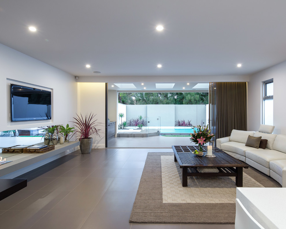 Inspiration for a contemporary open concept family room in Adelaide with white walls, a wall-mounted tv and grey floor.