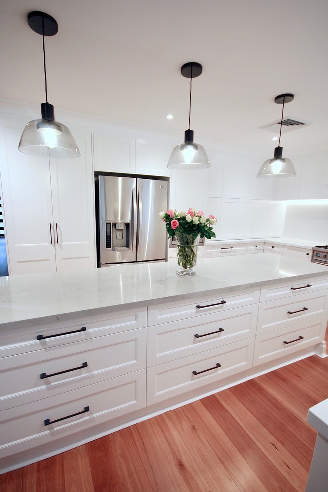 Photo of a large transitional u-shaped eat-in kitchen in Sydney with an undermount sink, recessed-panel cabinets, white cabinets, quartz benchtops, white splashback, stone slab splashback, stainless steel appliances, medium hardwood floors, with island, brown floor and white benchtop.