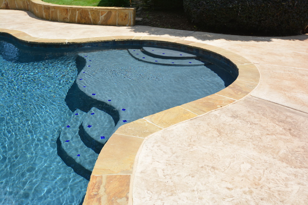 Photo of a large traditional backyard custom-shaped pool in Little Rock with a water feature and stamped concrete.
