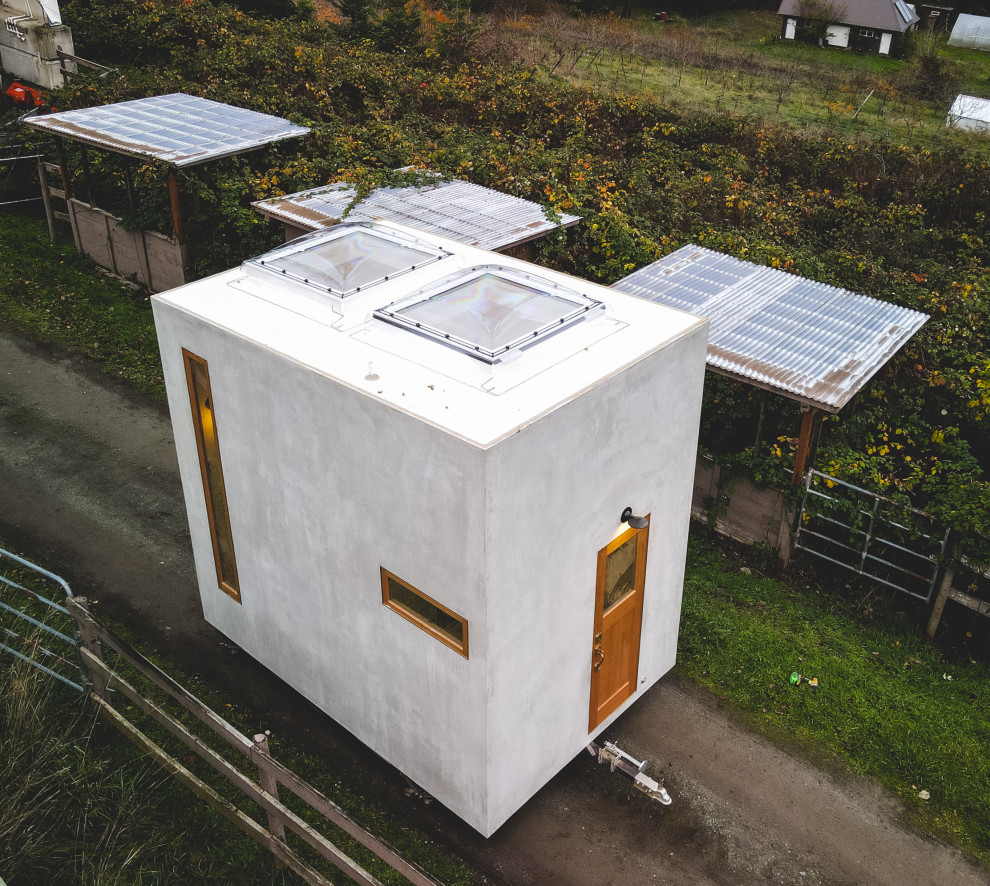 Kleines, Einstöckiges Modernes Tiny House mit Betonfassade, grauer Fassadenfarbe, Flachdach und weißem Dach in Sonstige