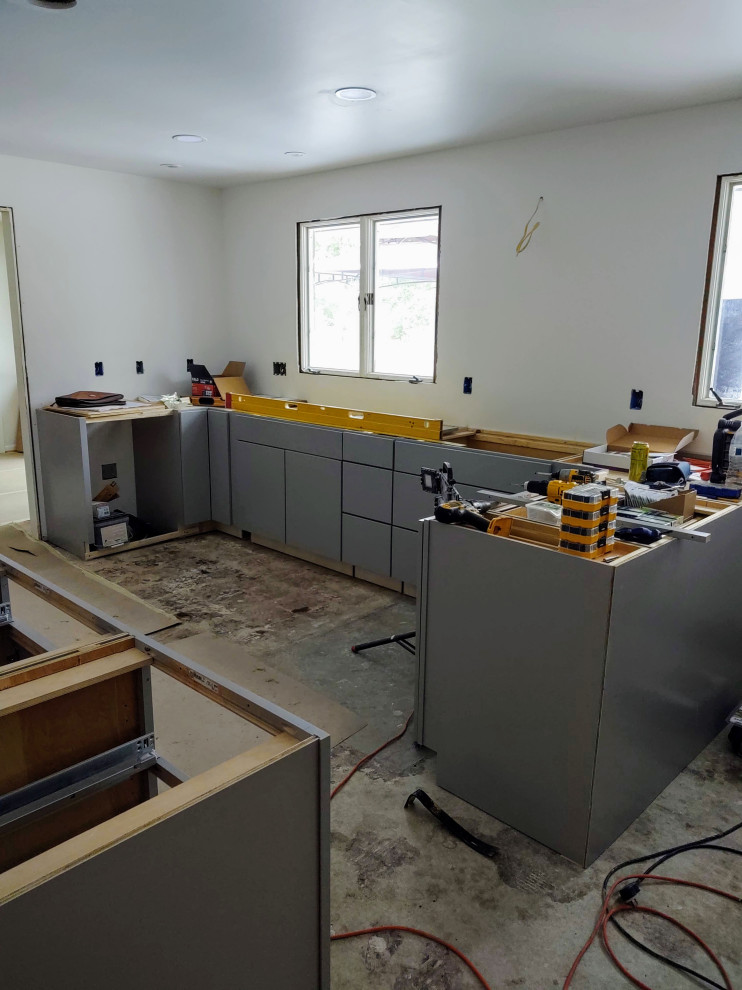 Example of a mid-sized u-shaped enclosed kitchen design with flat-panel cabinets, gray cabinets and a peninsula