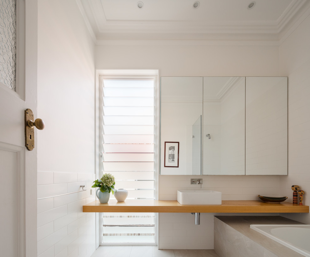 Mid-sized contemporary kids bathroom in Sydney with furniture-like cabinets, light wood cabinets, a drop-in tub, a shower/bathtub combo, white tile, ceramic tile, white walls, ceramic floors, a console sink, marble benchtops and beige floor.