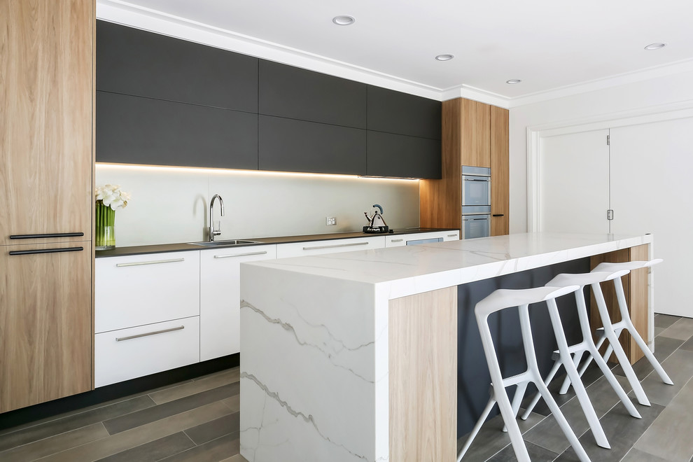 Design ideas for a large contemporary single-wall open plan kitchen in Sydney with a drop-in sink, flat-panel cabinets, brown cabinets, quartz benchtops, metallic splashback, porcelain splashback, stainless steel appliances, porcelain floors, with island, brown floor and white benchtop.