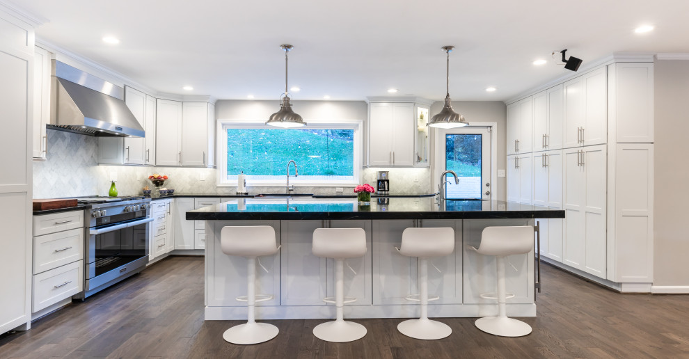 Photo of a medium sized classic kitchen/diner in DC Metro with a submerged sink, recessed-panel cabinets, white cabinets, grey splashback, stainless steel appliances, an island, brown floors and black worktops.