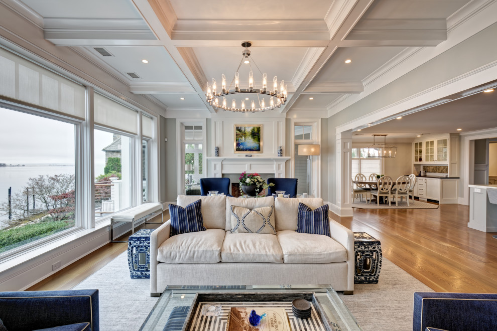 Large beach style formal open concept living room in New York with grey walls, light hardwood floors, a wood fireplace surround, a built-in media wall, grey floor, coffered and a two-sided fireplace.