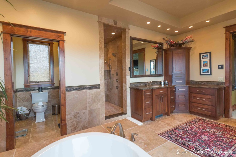 Inspiration for a large country master bathroom in Other with shaker cabinets, dark wood cabinets, a drop-in tub, a corner shower, a one-piece toilet, beige tile, brown tile, ceramic tile, beige walls, travertine floors, an undermount sink and soapstone benchtops.