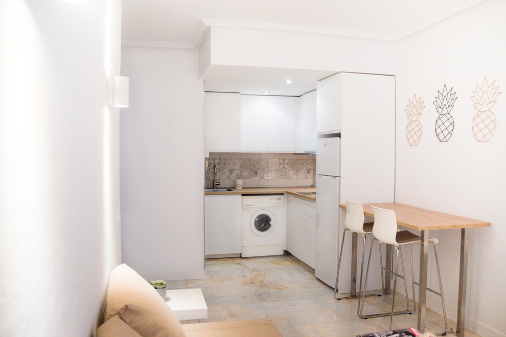 Small scandinavian l-shaped open plan kitchen in Madrid with a single-bowl sink, flat-panel cabinets, white cabinets, laminate benchtops, beige splashback, ceramic splashback, white appliances, marble floors, no island, white floor and brown benchtop.