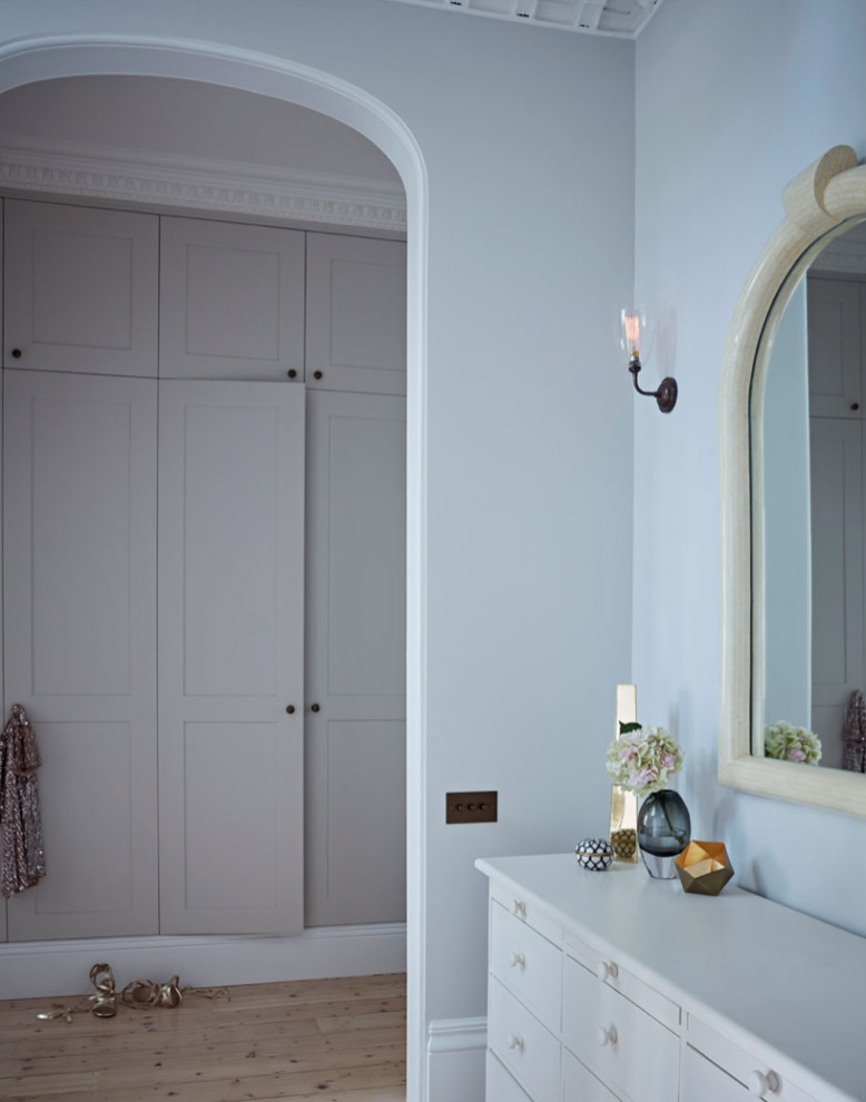 This is an example of a large transitional gender-neutral dressing room in London with shaker cabinets, beige cabinets and light hardwood floors.