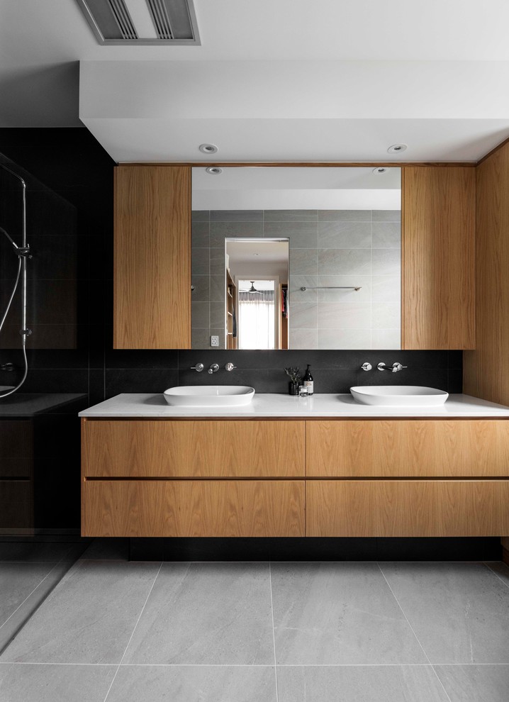 Large contemporary master bathroom in Brisbane with medium wood cabinets, black tile, white benchtops, flat-panel cabinets, a curbless shower, black walls, a vessel sink and grey floor.