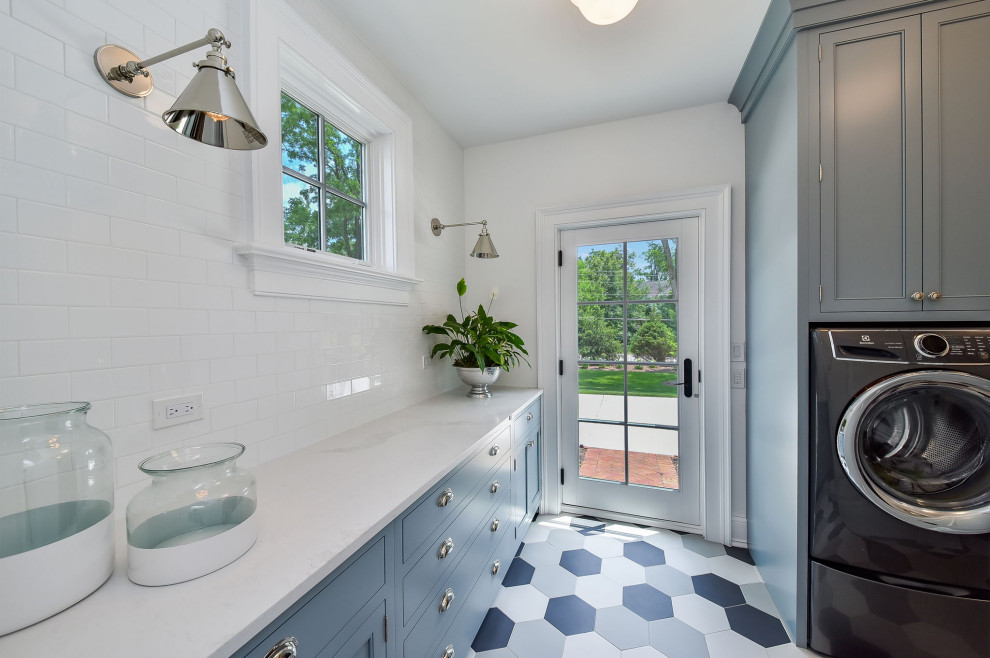 Photo of a large transitional dedicated laundry room in Chicago with a farmhouse sink, flat-panel cabinets, blue cabinets, quartz benchtops, white splashback, subway tile splashback, white walls, ceramic floors, a side-by-side washer and dryer, blue floor and white benchtop.