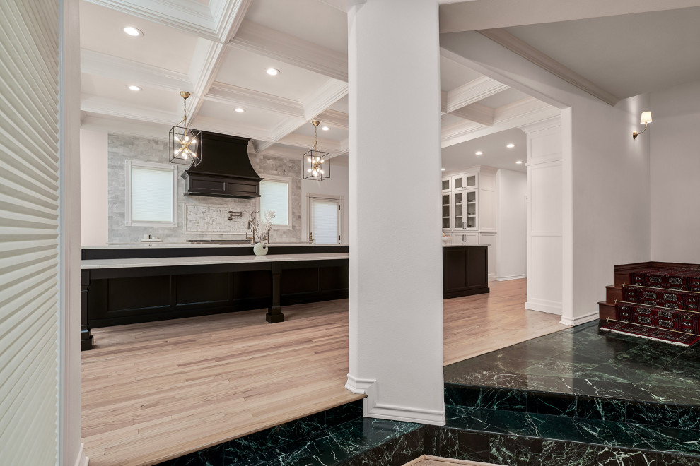 Photo of an expansive traditional kitchen/diner in Austin with a belfast sink, recessed-panel cabinets, white cabinets, engineered stone countertops, grey splashback, marble splashback, black appliances, light hardwood flooring, multiple islands, brown floors, white worktops and a coffered ceiling.