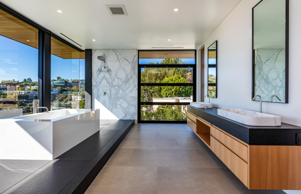 Contemporary master bathroom in Orange County with flat-panel cabinets, light wood cabinets, a freestanding tub, an open shower, multi-coloured tile, stone slab, white walls, a vessel sink, grey floor, an open shower, black benchtops and a double vanity.