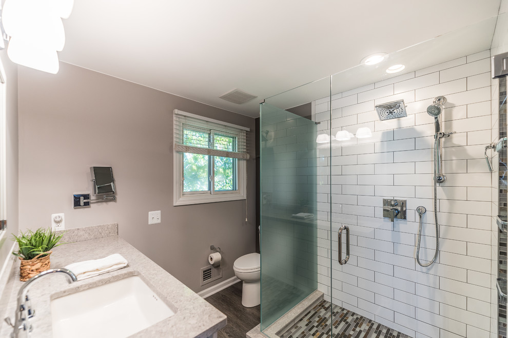 Design ideas for a mid-sized contemporary master bathroom in Detroit with flat-panel cabinets, grey cabinets, a corner shower, a two-piece toilet, white tile, glass sheet wall, grey walls, vinyl floors, an undermount sink, glass benchtops, multi-coloured floor, a hinged shower door and grey benchtops.