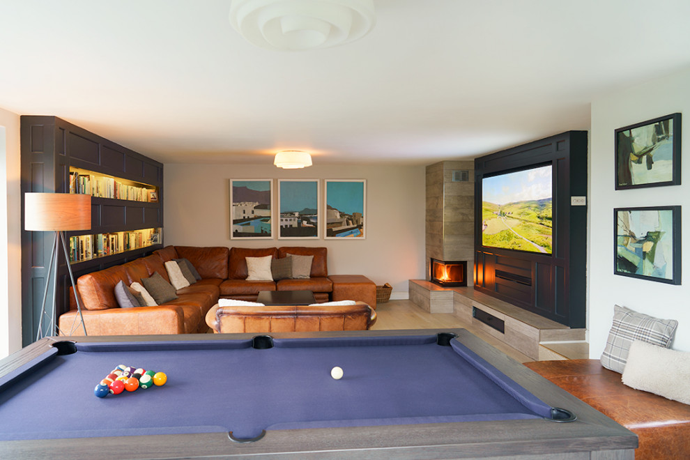 Immagine di un grande soggiorno minimalista aperto con sala giochi, pareti grigie, parquet chiaro, camino ad angolo, cornice del camino piastrellata e TV a parete