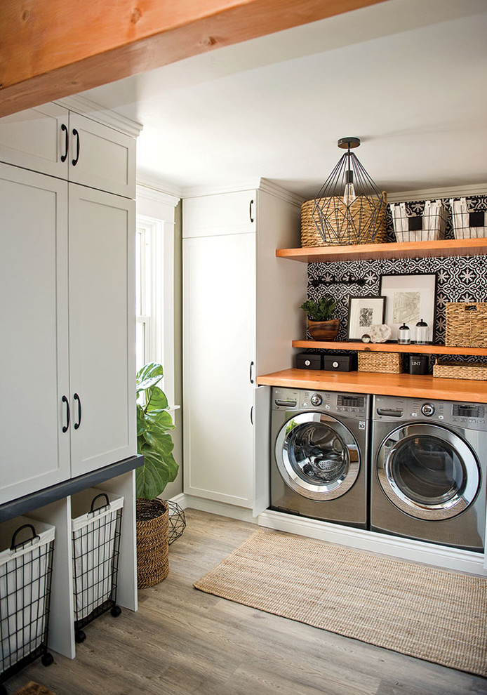 Inspiration for a small country u-shaped utility room in Other with shaker cabinets, white cabinets, wood benchtops, white walls, vinyl floors, a side-by-side washer and dryer, grey floor and brown benchtop.