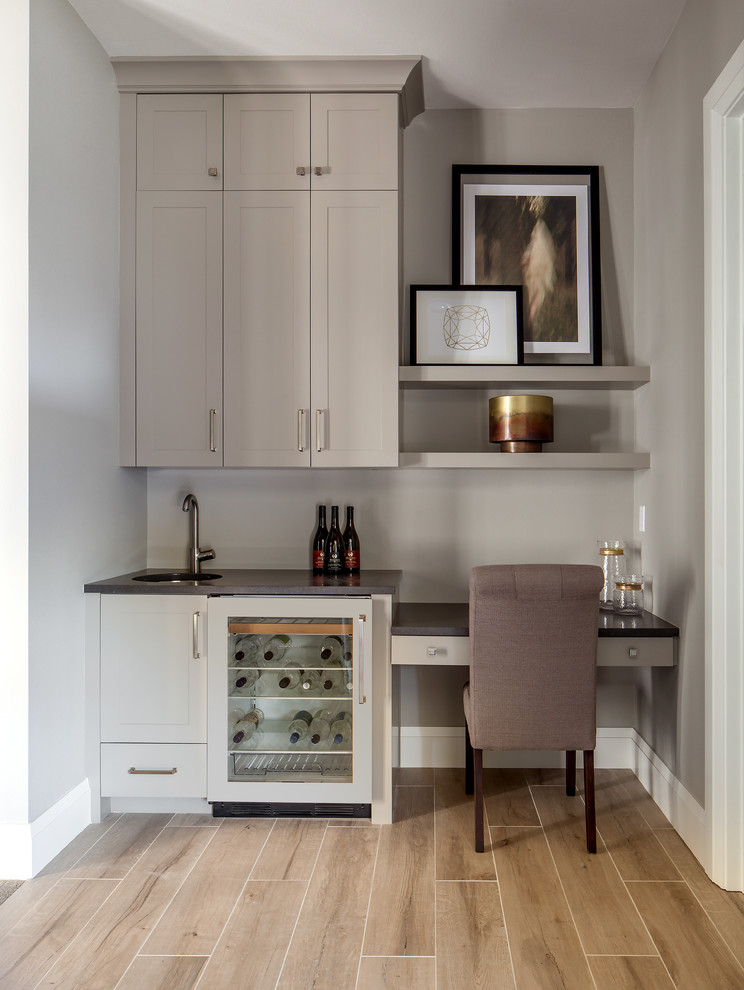 Mid-sized country single-wall wet bar with an undermount sink, shaker cabinets, beige cabinets, quartz benchtops, beige splashback, porcelain floors and brown floor.