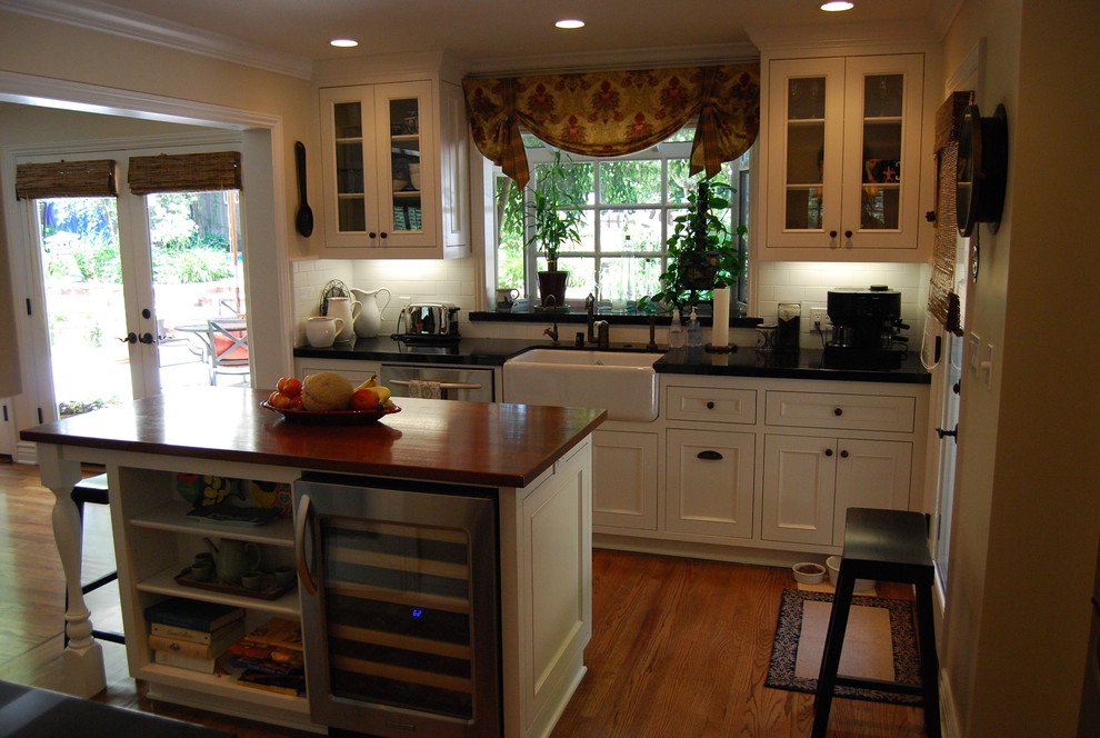 This is an example of a traditional l-shaped eat-in kitchen in Los Angeles with a farmhouse sink, beaded inset cabinets, white cabinets, soapstone benchtops, white splashback, subway tile splashback and stainless steel appliances.