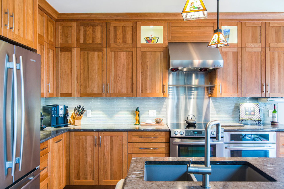 This is an example of a traditional l-shaped eat-in kitchen in Montreal with an undermount sink, shaker cabinets, medium wood cabinets, granite benchtops, white splashback and stainless steel appliances.