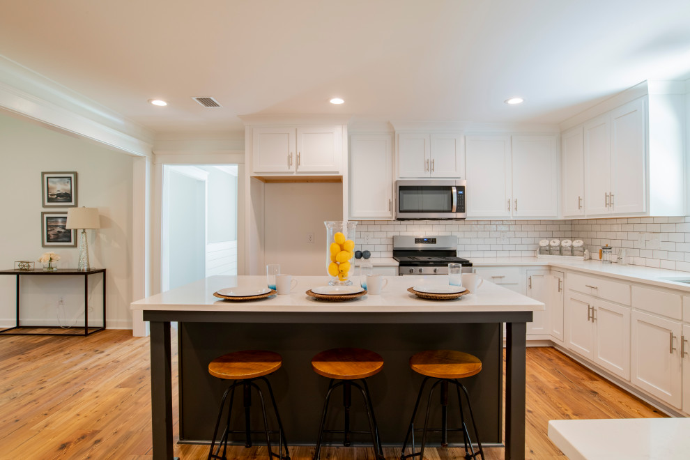 Inspiration for an u-shaped medium tone wood floor and brown floor kitchen remodel with an undermount sink, shaker cabinets, white cabinets, granite countertops, white backsplash, subway tile backsplash, stainless steel appliances, an island and white countertops