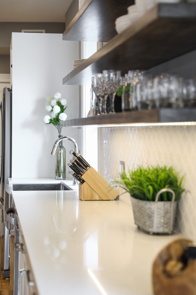 Example of a mid-sized transitional single-wall medium tone wood floor and brown floor eat-in kitchen design with a farmhouse sink, shaker cabinets, white cabinets, white backsplash, stainless steel appliances, an island and white countertops