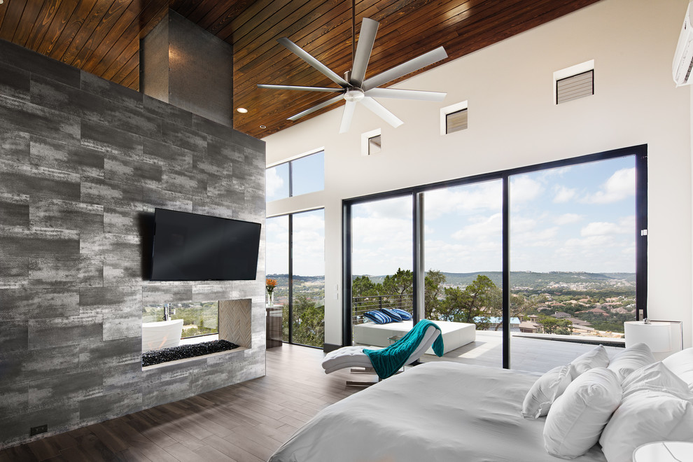 Photo of a large modern master bedroom in Austin with white walls, ceramic floors, a two-sided fireplace, a metal fireplace surround and brown floor.