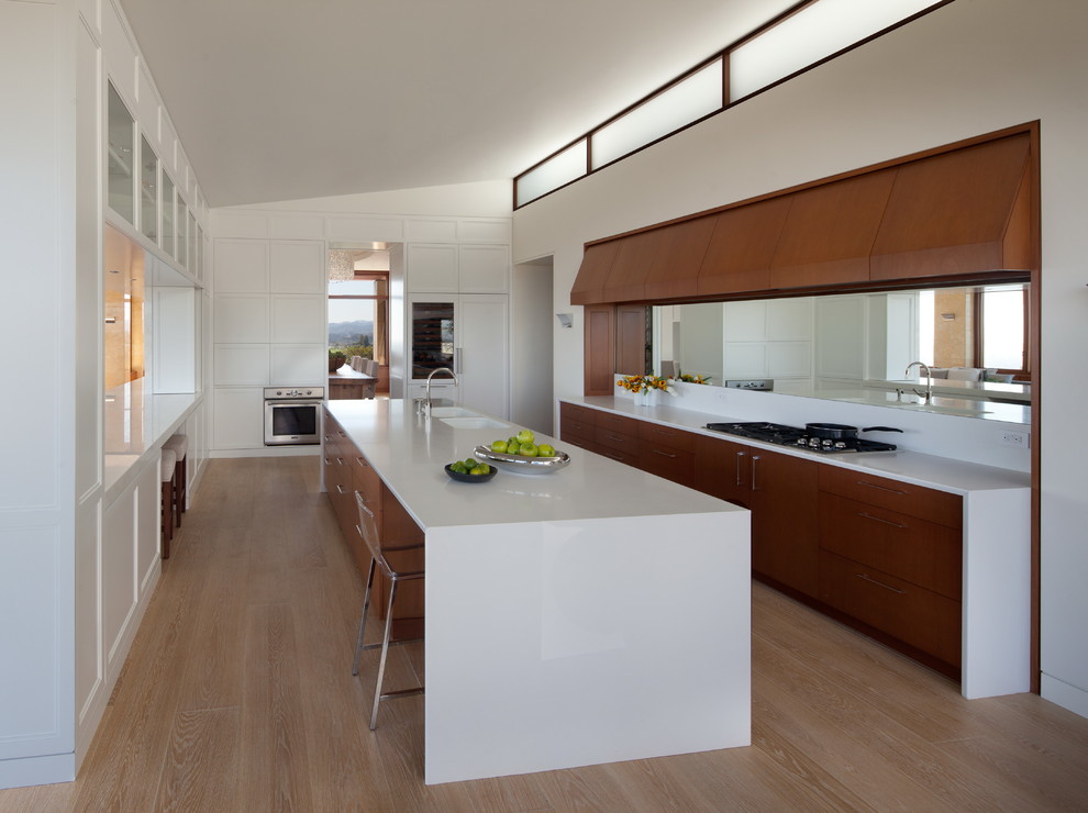 Mid-sized transitional u-shaped eat-in kitchen in Los Angeles with medium wood cabinets, with island, an integrated sink, flat-panel cabinets, quartz benchtops, white splashback, mirror splashback, stainless steel appliances and medium hardwood floors.