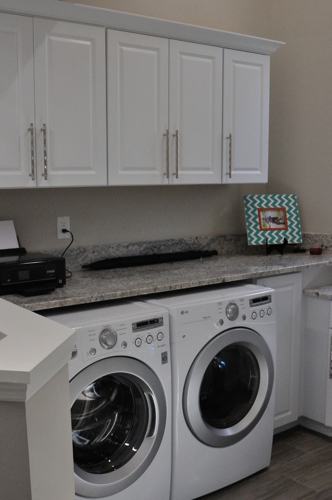 Photo of a small traditional single-wall laundry cupboard in Miami with raised-panel cabinets, yellow cabinets, granite benchtops, grey walls, medium hardwood floors, a side-by-side washer and dryer, brown floor and grey benchtop.