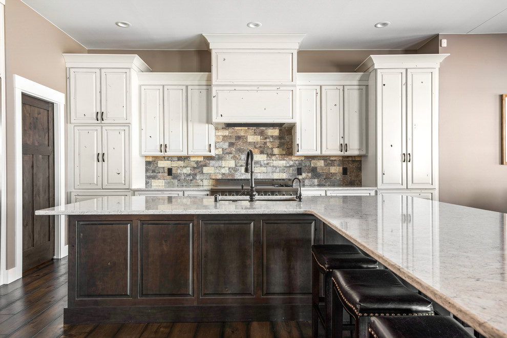 Eat-in kitchen - large transitional l-shaped medium tone wood floor and brown floor eat-in kitchen idea with an undermount sink, raised-panel cabinets, quartz countertops, beige backsplash, stone tile backsplash, stainless steel appliances, an island and beige countertops