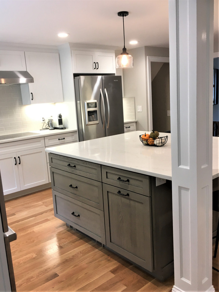 Eat-in kitchen - large transitional u-shaped light wood floor and brown floor eat-in kitchen idea in Boston with a farmhouse sink, shaker cabinets, white cabinets, quartz countertops, beige backsplash, subway tile backsplash, stainless steel appliances, an island and white countertops