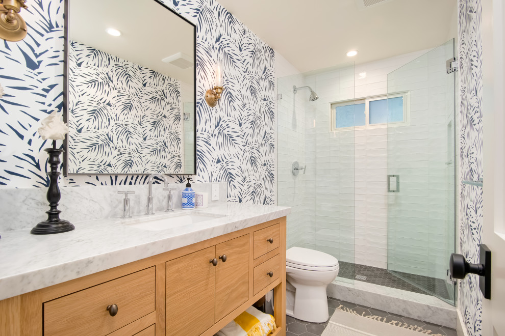 Inspiration for a beach style 3/4 bathroom in Orange County with flat-panel cabinets, medium wood cabinets, an alcove shower, a two-piece toilet, white tile, multi-coloured walls, an undermount sink, grey floor, a hinged shower door and grey benchtops.