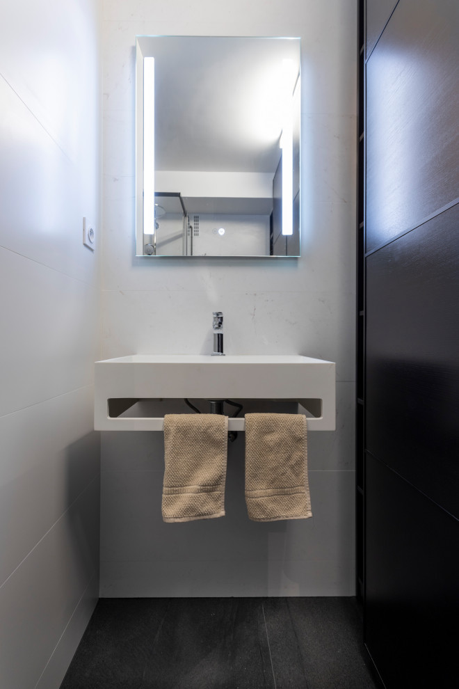 Photo of a small contemporary grey and black shower room bathroom in Paris with beaded cabinets, black cabinets, a corner shower, a one-piece toilet, white tiles, ceramic tiles, white walls, ceramic flooring, a console sink, solid surface worktops, black floors, a sliding door, white worktops, a laundry area, a single sink and a built in vanity unit.