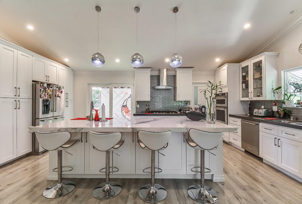 Design ideas for a transitional u-shaped kitchen in Los Angeles with an undermount sink, shaker cabinets, white cabinets, grey splashback, glass tile splashback, stainless steel appliances, light hardwood floors, with island, beige floor and grey benchtop.