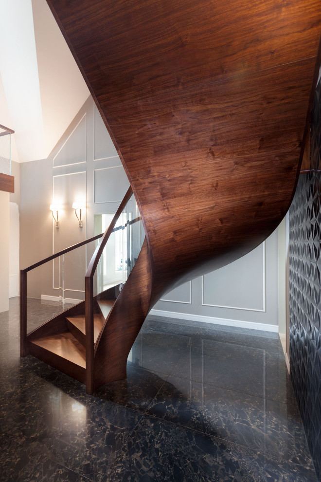 На фото: изогнутая деревянная лестница в современном стиле с деревянными ступенями и стеклянными перилами с