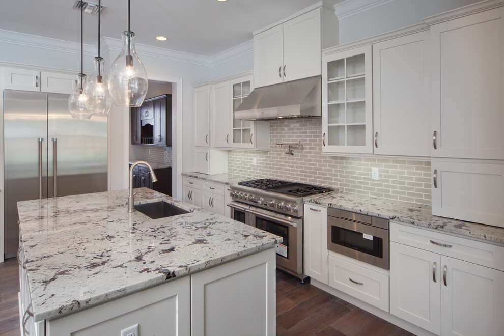 Photo of a large traditional galley open plan kitchen in Orlando with a drop-in sink, flat-panel cabinets, white cabinets, granite benchtops, grey splashback, subway tile splashback, stainless steel appliances, dark hardwood floors and multiple islands.