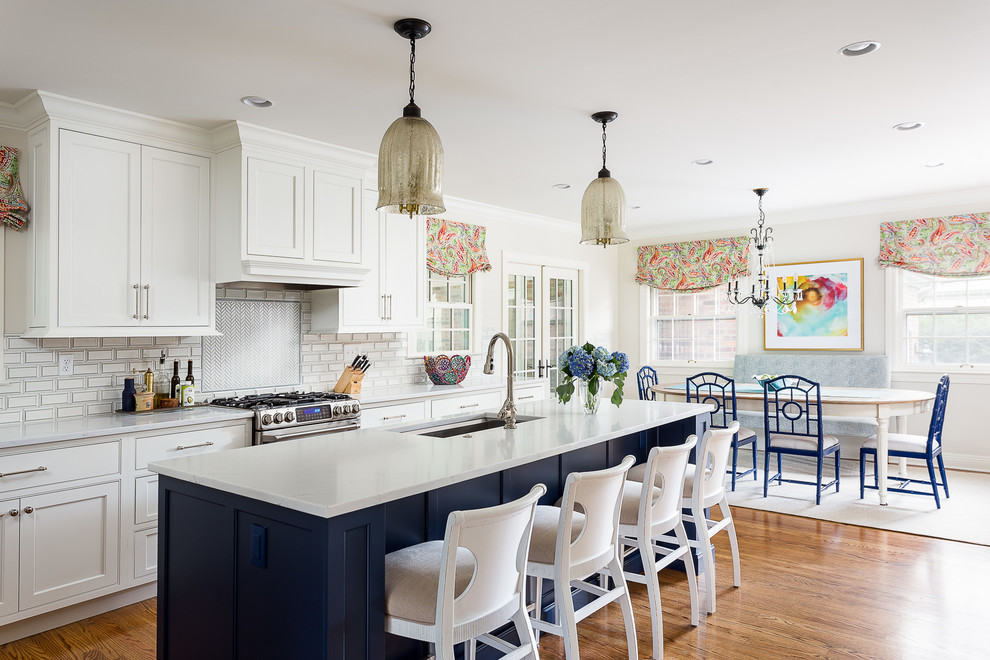 This is an example of a mid-sized beach style eat-in kitchen in Louisville with a single-bowl sink, white cabinets, quartz benchtops, white splashback, ceramic splashback, stainless steel appliances, with island, brown floor, white benchtop, medium hardwood floors and beaded inset cabinets.