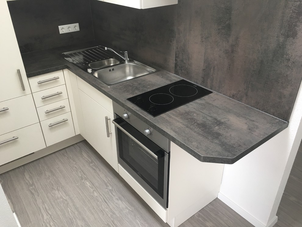 Küche ohne Insel in L-Form mit integriertem Waschbecken, flächenbündigen Schrankfronten, weißen Schränken, Laminat-Arbeitsplatte, Küchenrückwand in Metallic, Rückwand aus Holz, Küchengeräten aus Edelstahl, dunklem Holzboden und grauem Boden
