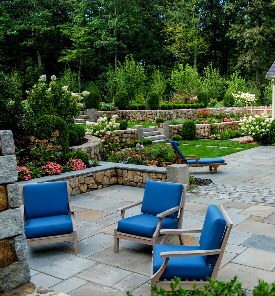 This is an example of a mid-sized traditional backyard full sun garden in Boston with a retaining wall and natural stone pavers.