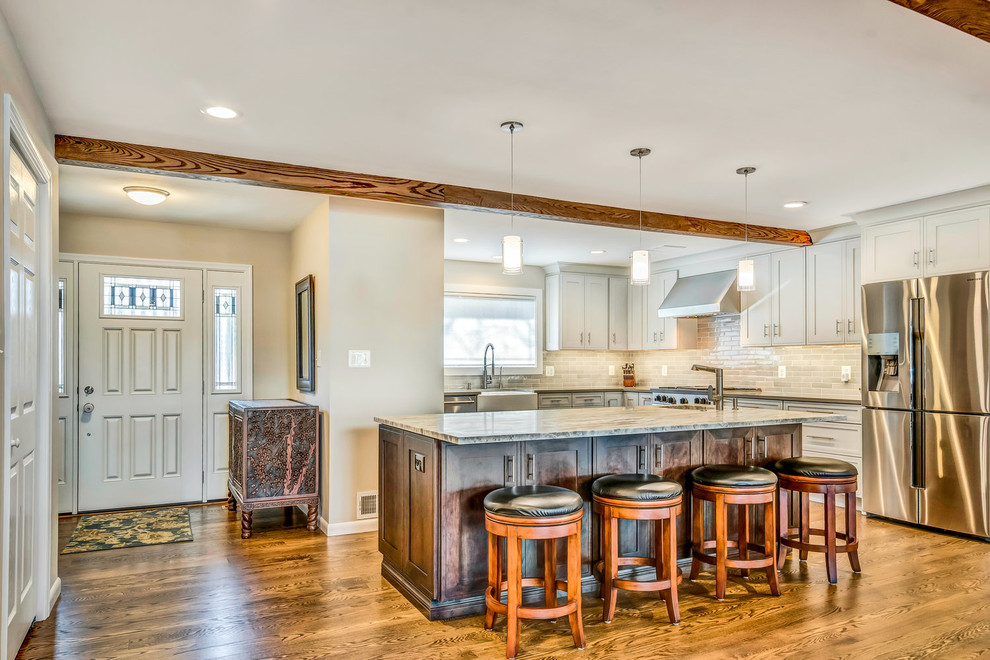 Transitional medium tone wood floor and brown floor eat-in kitchen photo in DC Metro with a farmhouse sink, shaker cabinets, white cabinets, granite countertops, white backsplash, subway tile backsplash, stainless steel appliances, an island and multicolored countertops
